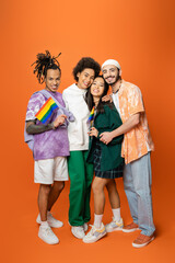 full length of stylish and cheerful multicultural friends embracing while holding lgbt flags on...