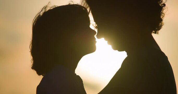 Close up face of woman and boy in profile at warm orange dawn. Mother and son rub their noses and say important supportive and loving words to each other. Love in moment of unity of mother and son