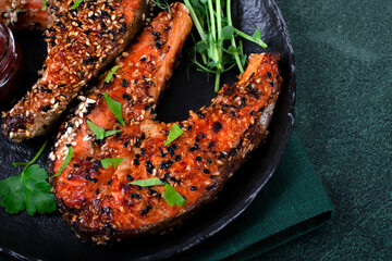 Fried trout steak served with sesame seeds on dark plate. Close-up - 574977700