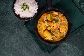 Fish curry with codfish, pollack and shrimps with coconut milk served in cast iron pan and bowl of...