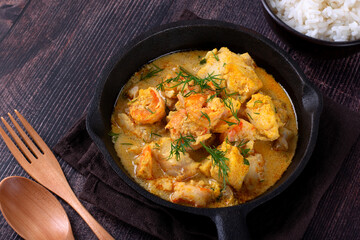 Fish curry with codfish, pollack and shrimps with coconut milk served in cast iron pan - 574977713