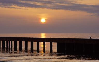 Fototapeta na wymiar sunset under a cloudy sky with a pier