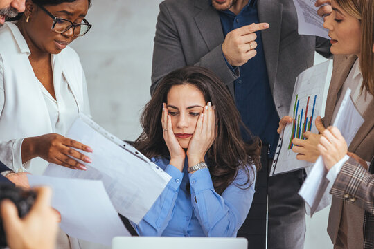 Frustrated Millennial Female Worker Sitting At Table With Colleagues, Felling Tired Of Working Quarreling At Business Meeting. Upset Stressed Young Businesswoman Suffering From Head Ache At Office.