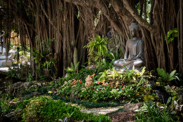 Estatua de buda meditando en jardín natural, dentro de templo budista tailandes