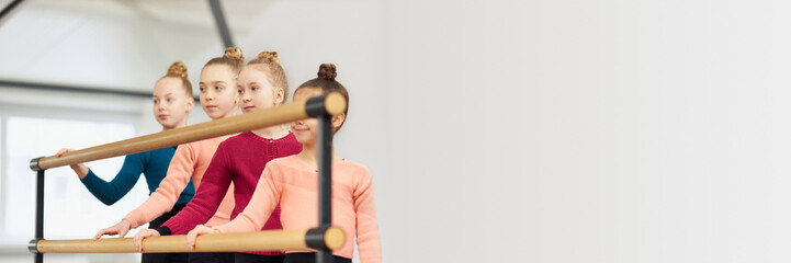 Group of little girls, children, gymnasts training indoors. Stretching exercises with barre equipment. Concept of sportive lifestyle, childhood, education, health, professional sport. Banner