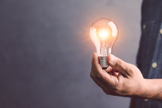 Businessman holding a clear light bulb with light effect on gray space wall background. Concept of new ideas for work.