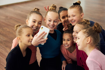 Group of beautiful little girls, children, rhythmic gymnasts doing selfie with phone after training session indoors. Friendly team. Sportive lifestyle, childhood, education, professional sport.