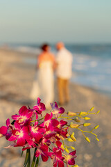 Bride and groom walking away out of focus in background with bridal bouquet in the foreground on sandy beach