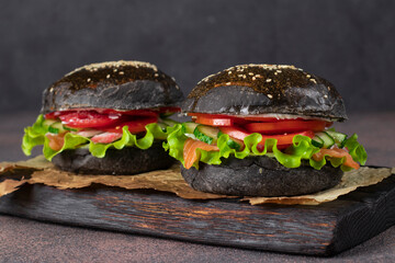 Two veggie black burger with salted salmon, crab meat and vegetables on wooden board on brown background