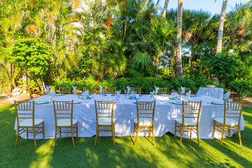 Dinner table and chairs for small group outdoors on green grass surrounded by green landscape.