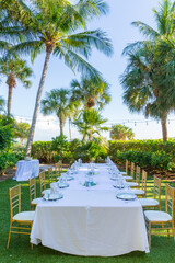 Dinner table and chairs for small group, next to the beach surrounded by palm trees.