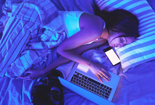 Woman, night and technology while sleeping in home bed with light from laptop and phone in bedroom. Tired student person with burnout asleep online for remote work or mockup social media chat on top