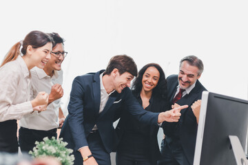 A team of exclusive diversity businesspeople are gathered together in an office, excitedly watching their accomplishment on a laptop computer. Idea for fostering strong teamwork in the workplace.