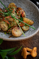 Fried potatoes with chanterelles and green onions in a gray bowl. Vegan dish with potatoes and mushrooms, selective focus, close up
