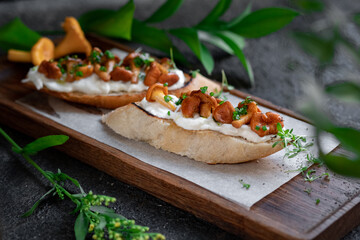Bruschetta with chanterelles and Philadelphia cream cheese on a wooden board. Mushroom sandwich decorated with greens, close up
