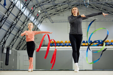 Little girl, child, rhythmic gymnast training indoors with coach, doing exercise with ribbon....