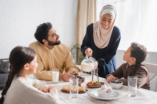 African American Woman In Hijab Pouring Milk Near Family During Suhur Breakfast At Home.