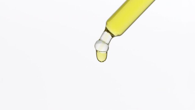 Chamomile extract is dripping from lab dropper occasionally on grey background | Abstract skin care serum formulation concept