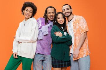 happy multiethnic friends wearing stylish clothes and posing isolated on orange.