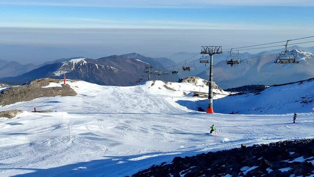 V&iacute;deo panor&acirc;mico com uma pista de neve e com alguns esquiadores a descer montanha abaixo enquanto o telef&eacute;rico sobe com mais esquiadores para o alto em Pierre Saint Martin nos Piren&eacute;us, Fran&ccedil;a