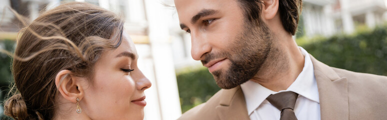 Obraz premium bearded man in suit looking at smiling bride outdoors, banner.