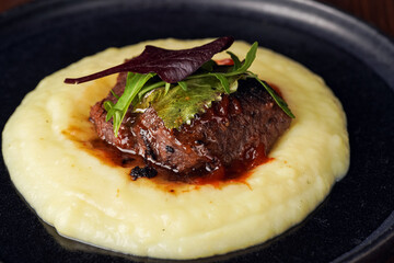 A medium rare ostrich steak in barbecue sauce on a cloud of herb mashed potato topped with fresh...