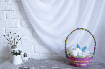 A colorful wicker Easter basket with eggs is on the table in the kitchen. The ears of a hare stick out of the basket. High quality photo