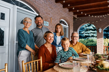 Happy multigeneration family at dining table on patio looking at camera.