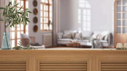 Wooden table top, cabinet, panel or shelf with shutters close up. Olive branch in vase and candles. Blurred background with boho living room with rattan furniture, interior design