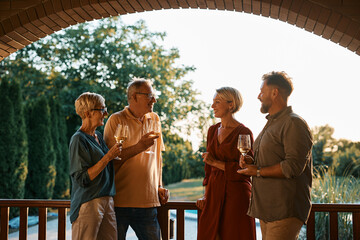 Happy couple and their senior parents talk while drinking wine on terrace.