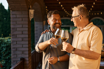 Happy man and his senior father toast with wine after family lunch on patio. - Powered by Adobe