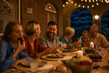 Happy man enjoys in family meal at dining table in evening on terrace.