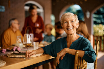 Happy senior woman enjoying at dining table with her extended family and looking at camera.