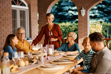 Happy woman having glass of wine while talking to her extended family during lunch on terrace.