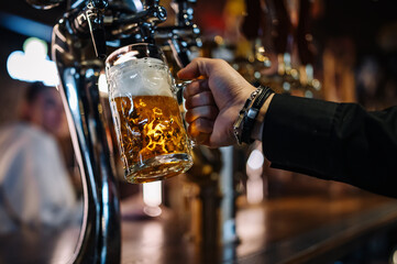 man bartender hand at beer tap pouring a draught beer in glass serving in a restaurant or pub