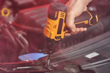 a man's hand unscrews a nut with a yellow battery wrench from a car