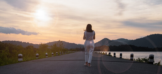 A picture of a young woman walking by a reservoir in the evening when the sun shines alone. give a feeling of loneliness