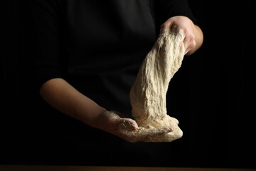 Fototapeta na wymiar Yeast dough in the hands of a cook on a black background.