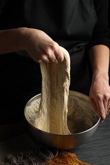 The hands of the cook knead the dough in a bowl on a black background.