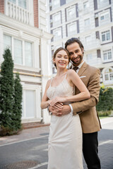 bearded man in suit with tie smiling and hugging happy bride in wedding dress.