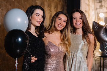 Close up portrait of adorable pretty happy girls with long hair and festive makeup going to camera with wonderful smiles and holding balloons over dark background 