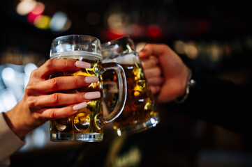 Two friends hands toasting with glasses of light beer at the pub or bar.