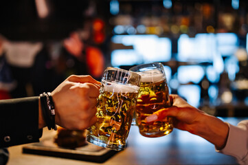 Fototapeta na wymiar Two friends hands toasting with glasses of light beer at the pub or bar.