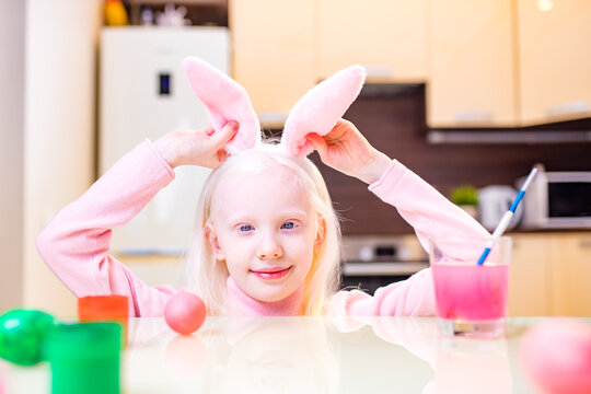 cute little girl painting easter eggs wear bunny ears in kitchen