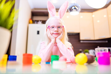 cute little girl painting easter eggs wear bunny ears in kitchen