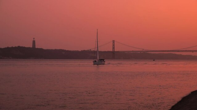 Sailing yacht floats on the river with a long suspension bridge in the evening at sunset