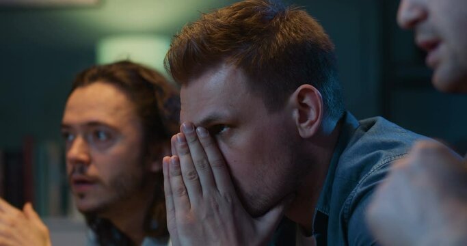 Close up of handsome Caucasian men football fans sitting on couch and watching football match late at night. Guys cheering and worrying for favorite team which missing goal and loosing in game.