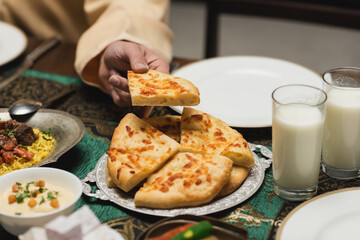 Cropped view of muslim man taking pita bread during ramadan dinner at home.