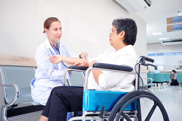Female doctor using a stethoscope examining an elderly female patient sitting on a wheelchair inside a hospital medical concept.