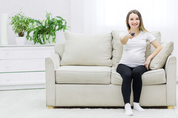 Fototapeta na wymiar Pregnant woman sitting on sofa with remote control.